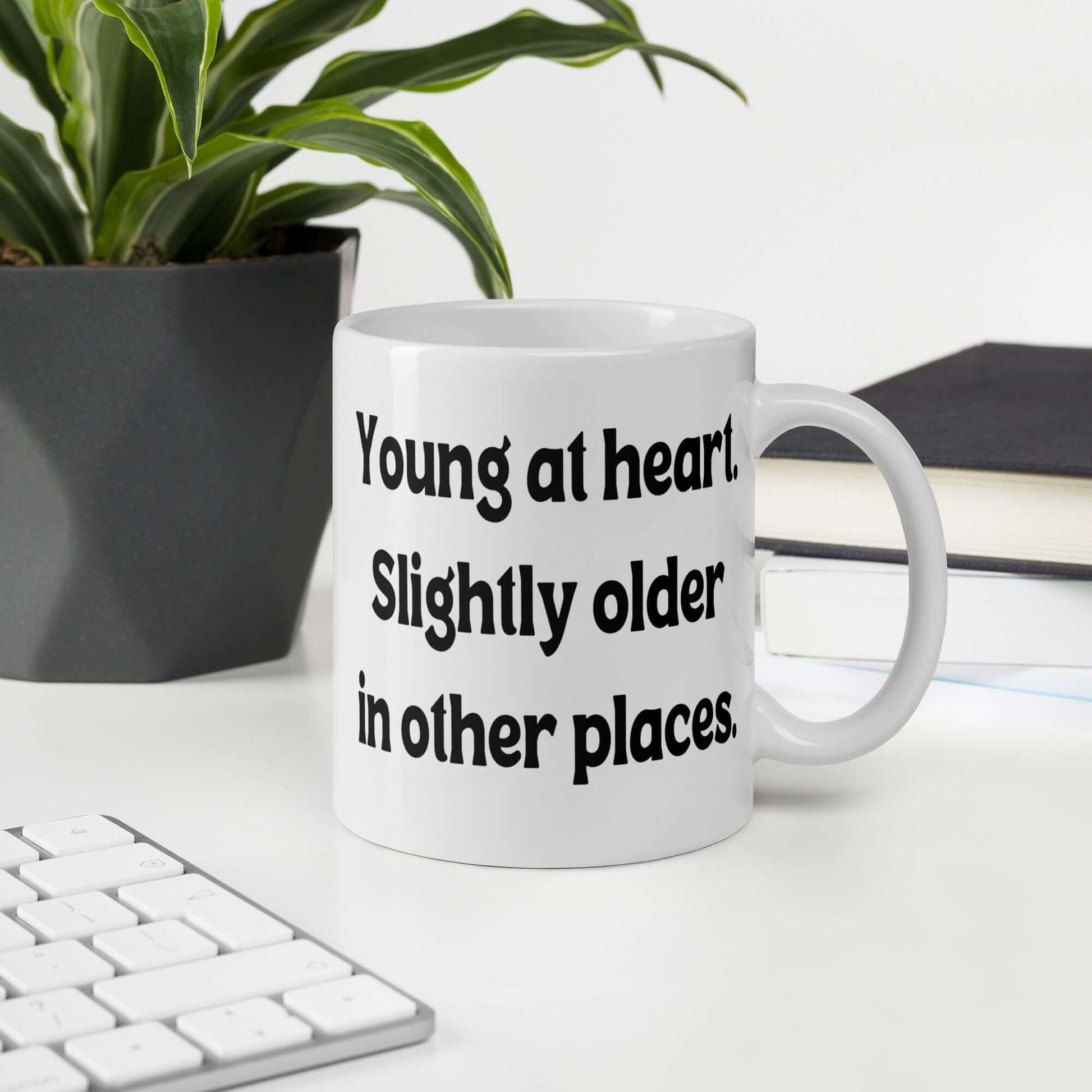 White ceramic mug with the words Young at heart, slightly older in other places printed on both sides.