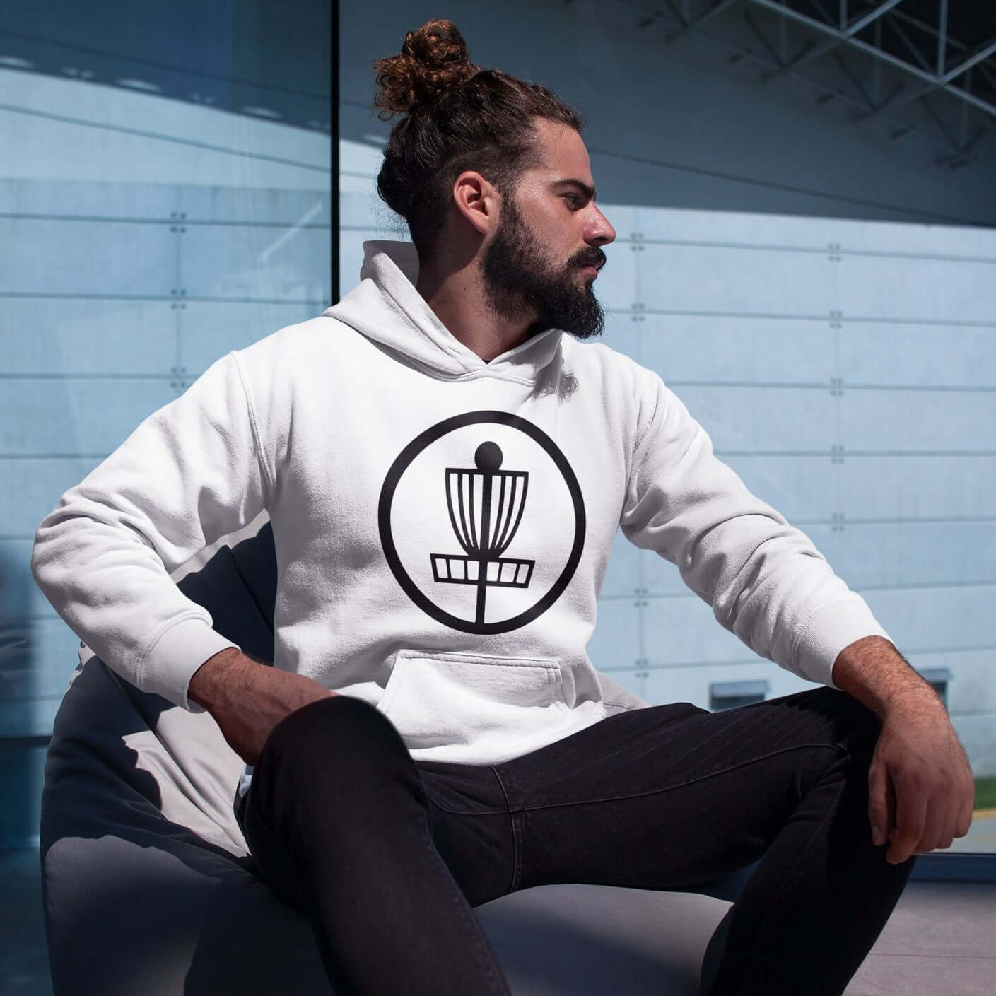 Man wearing white hoodie sweatshirt with image of disc golf basket silhouette with a circle around it printed on the front.