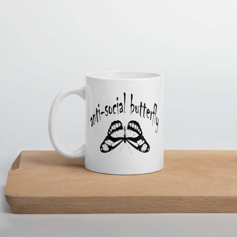 White ceramic coffee mug with an image of an upside down butterfly and the words Anti-social butterfly printed on both sides of the mug.