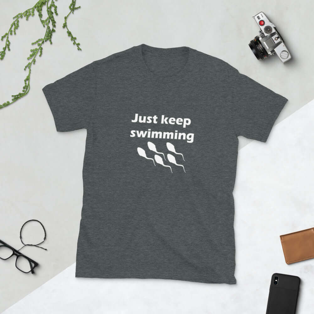 Dark heather grey t-shirt with the phrase Just keep swimming printed on the front. There is an image of some swimming sperm underneath the words.