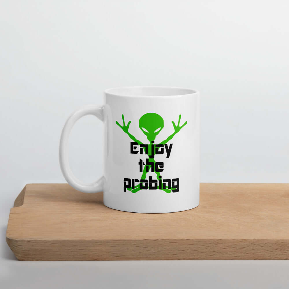 White ceramic coffee mug with an image of an alien and the funny phrase Enjoy the probing printed on both sides of the mug.