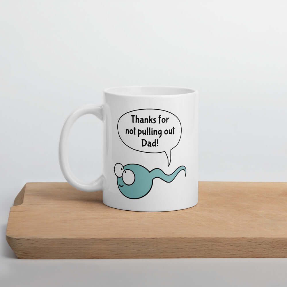 White ceramic coffee mug with an image of a smiling blue sperm with a word bubble that says Thanks for no pulling out Dad. The graphics are printed on both sides of the mug.