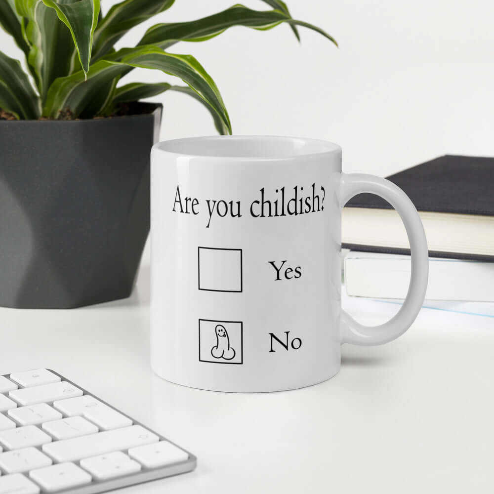 White ceramic coffee mug with the words Are you childish question mark. There are 2 check boxes to select Yes or No. There is a penis drawn inside of the No box. The graphics are printed on both sides of the mug.