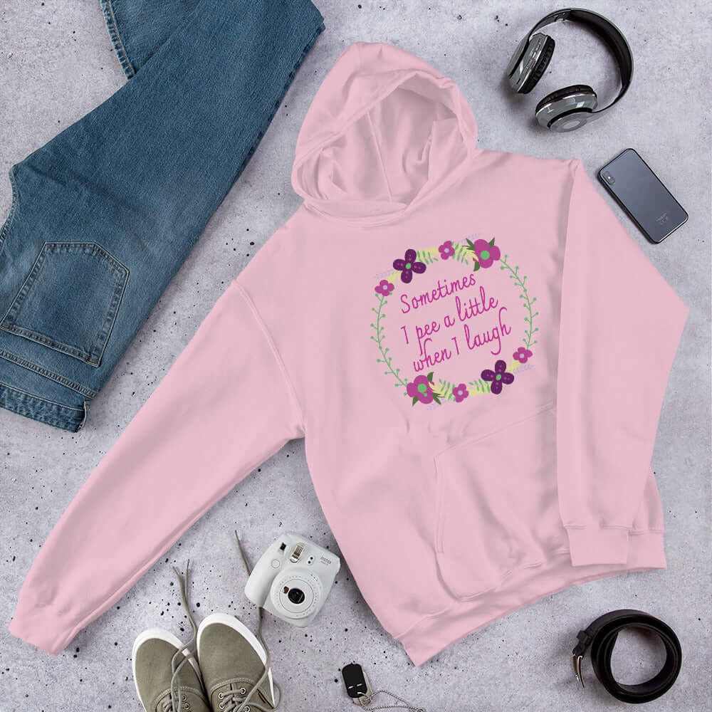 Light pink hoodie sweatshirt that has a minimalistic style line drawing floral wreath with the phrase Sometimes I pee a little when I laugh printed in the center of the wreath. The graphics are printed on the front of the hoodie.