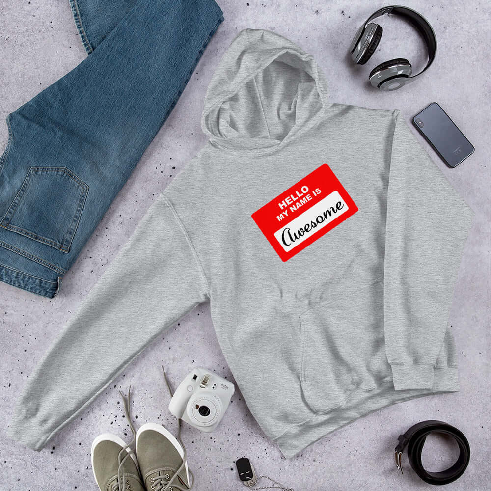 Light grey hoodie sweatshirt with an image of a classic red and white sticker name tag that says Hello my name is Awesome printed on the front.