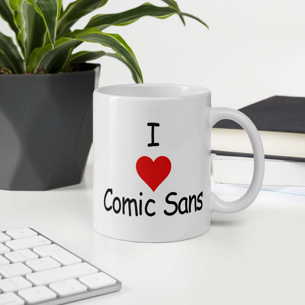 White ceramic coffee mug that says I heart Comic Sans on both sides of the mug. The text is in comic sans font.