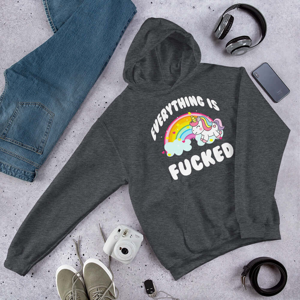Dark grey hoodie sweatshirt with a graphic of a kawaii style unicorn and a pastel rainbow with the words Everything is fucked printed on the front.