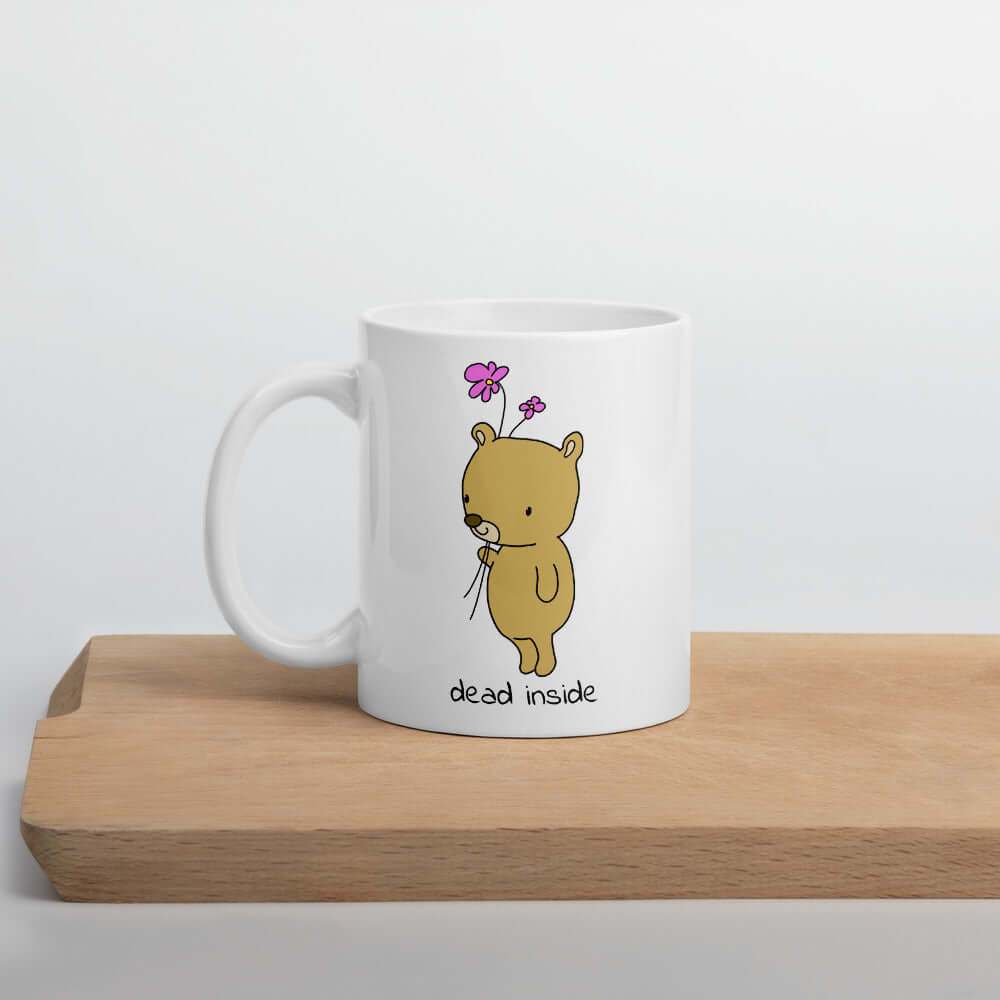 White ceramic coffee mug an image of a cute bear holding 2 pink flowers. The words Dead inside are printed underneath the bear. The graphics are printed on both sides of the mug.