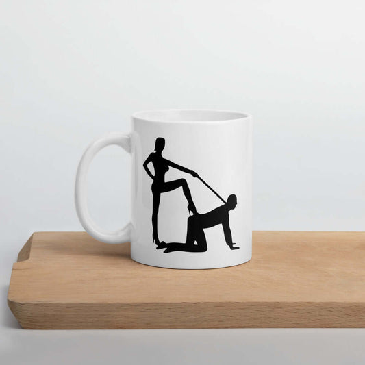 White ceramic coffee mug with the image of a silhouette of a man on his hands and knees and a dominatrix holding his leash printed on both sides.