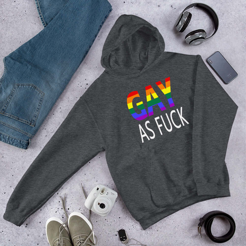 Dark heather grey hoodie sweatshirt with the words Gay as fuck printed on the front. The word Gay is in rainbow stripe font.