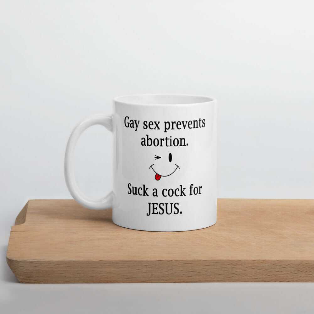 White ceramic coffee mug with the phrase Gay sex prevents abortion. Suck a cock for Jesus printed on both sides of the mug.