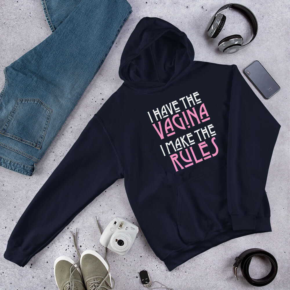 Navy blue hoodie sweatshirt with the words I have the vagina , I make the rules printed on the front. The words vagina and rules are pink, the rest of the words are white.