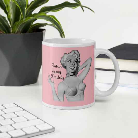 Pink and white ceramic coffee mug with an image of a retro black & white pin-up model and the phrase Satan is my Daddy printed on both sides.