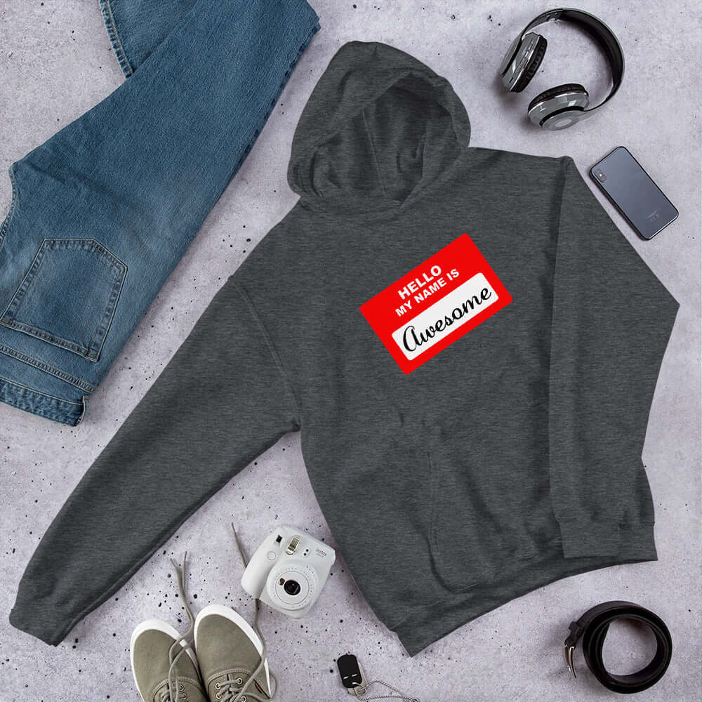 Dark heather grey hoodie sweatshirt with an image of a classic red and white sticker name tag that says Hello my name is Awesome printed on the front.