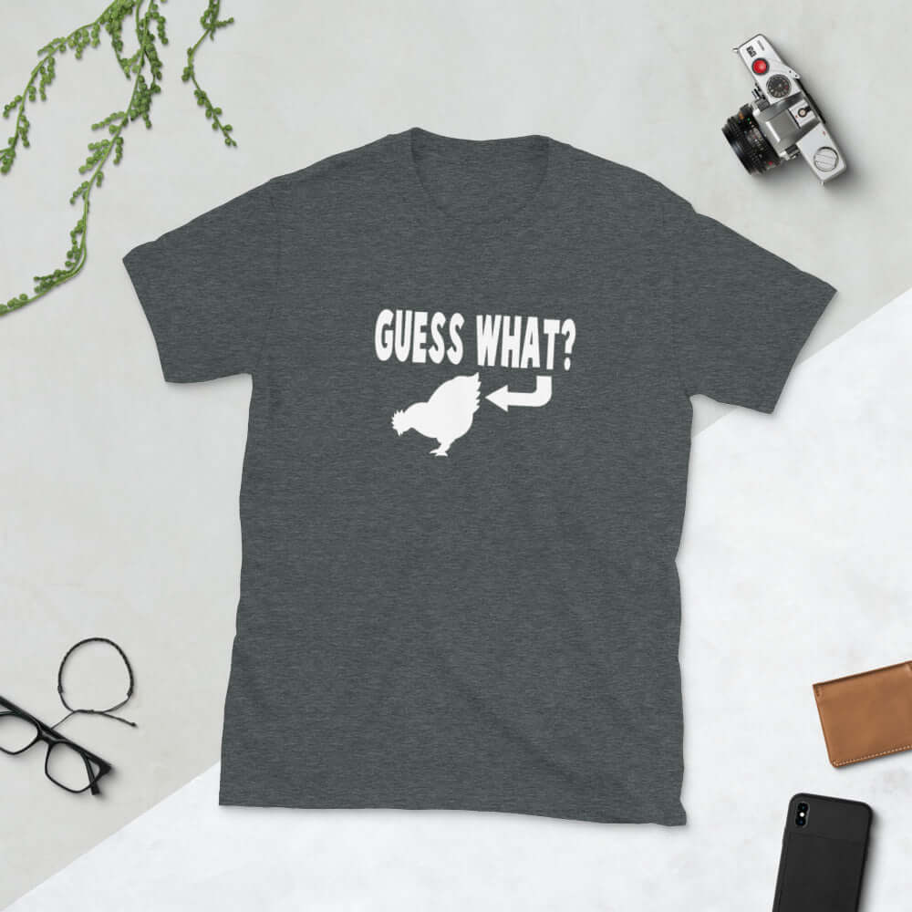 Dark heather grey t-shirt with an image of a chicken and the words Guess what question mark. There is an arrow pointing to the chickens butt. The graphics are printed on the front of the shirt.