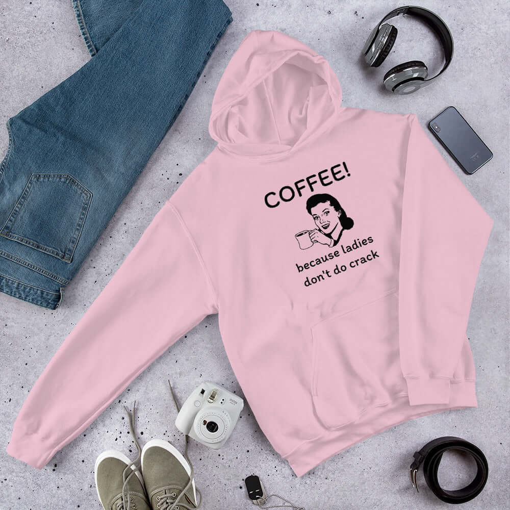 Light pink hoodie sweatshirt with an image of a retro woman holding a coffee mug with the phrase Coffee, because ladies don't do crack printed on the front.
