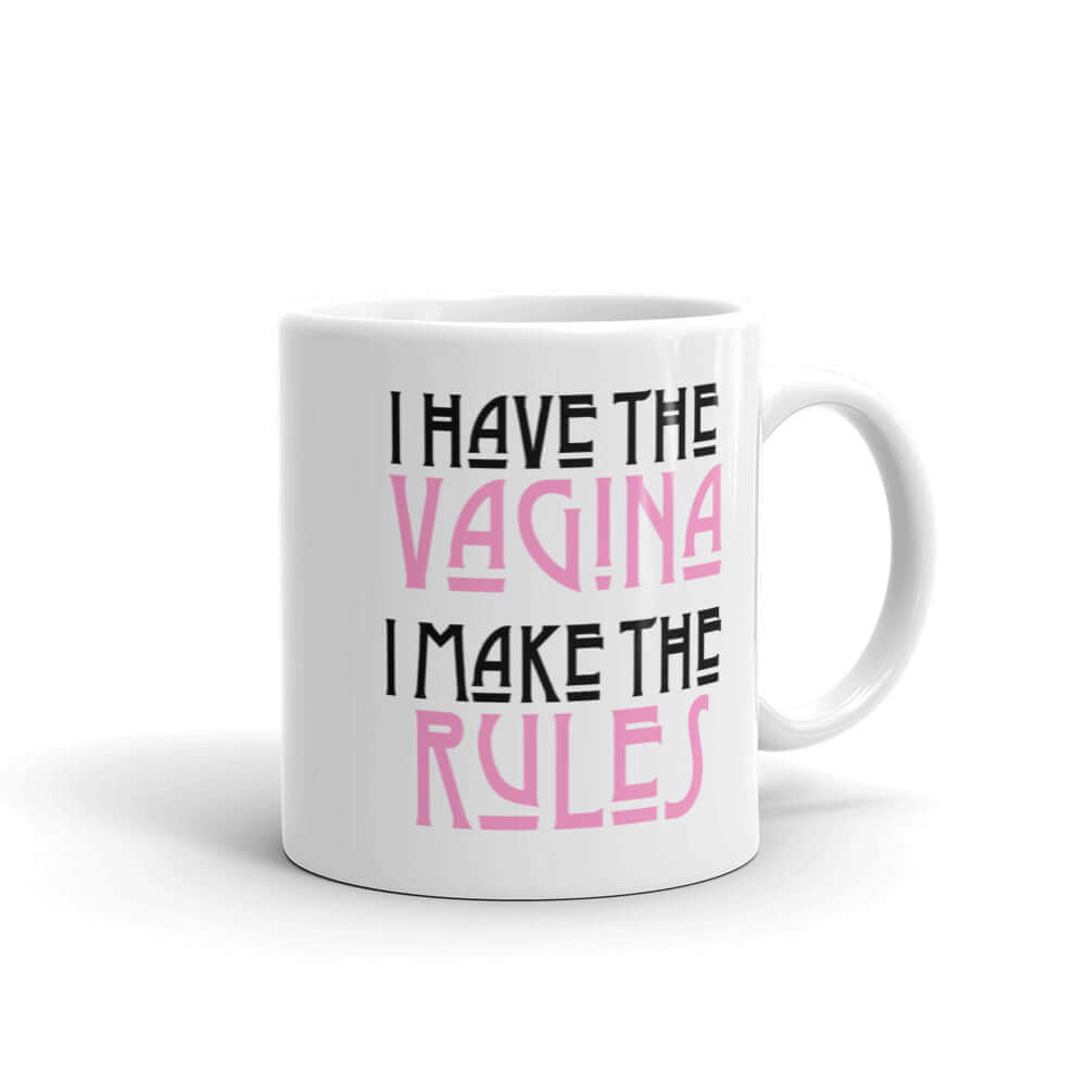 White ceramic coffee mug with the words I have the vagina , I make the rules printed on both sides. The words vagina and rules are pink, the rest of the words are black..