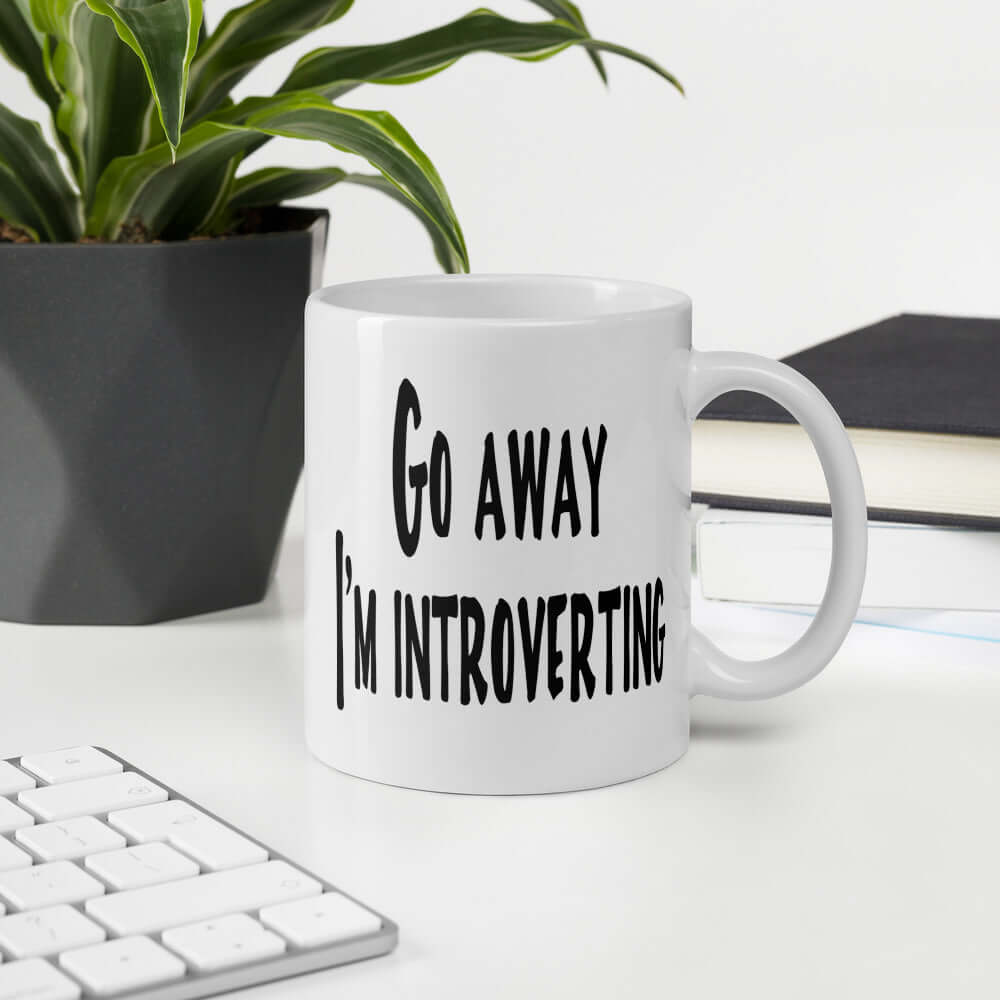 White ceramic coffee mug with the phrase Go away, I'm introverting printed on both sides of the mug.