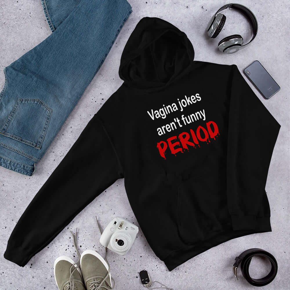 Black hoodie sweatshirt with the crude phrase Vagina jokes aren't funny...period. The word period is in a red drippy font. The graphics are printed on the front of the hoodie.