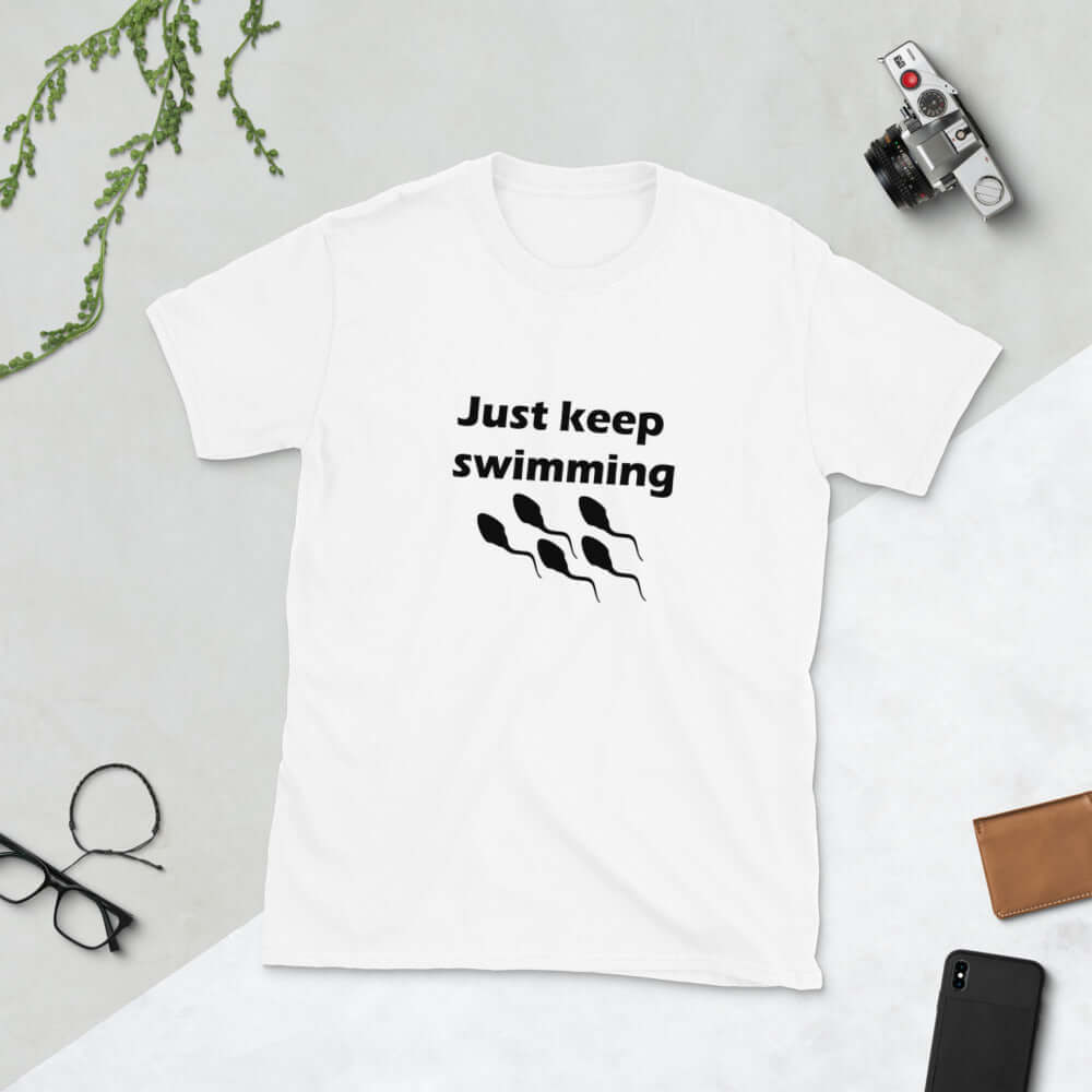 White t-shirt with the phrase Just keep swimming printed on the front. There is an image of some swimming sperm underneath the words.