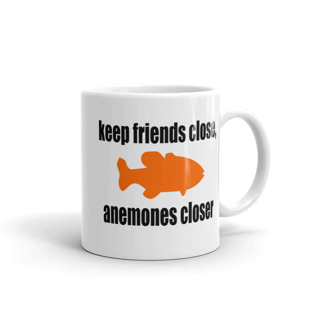 White ceramic coffee mug with the pun phrase Keep friends close, anemones closer with an image of an orange fish printed on both sides of the mug.