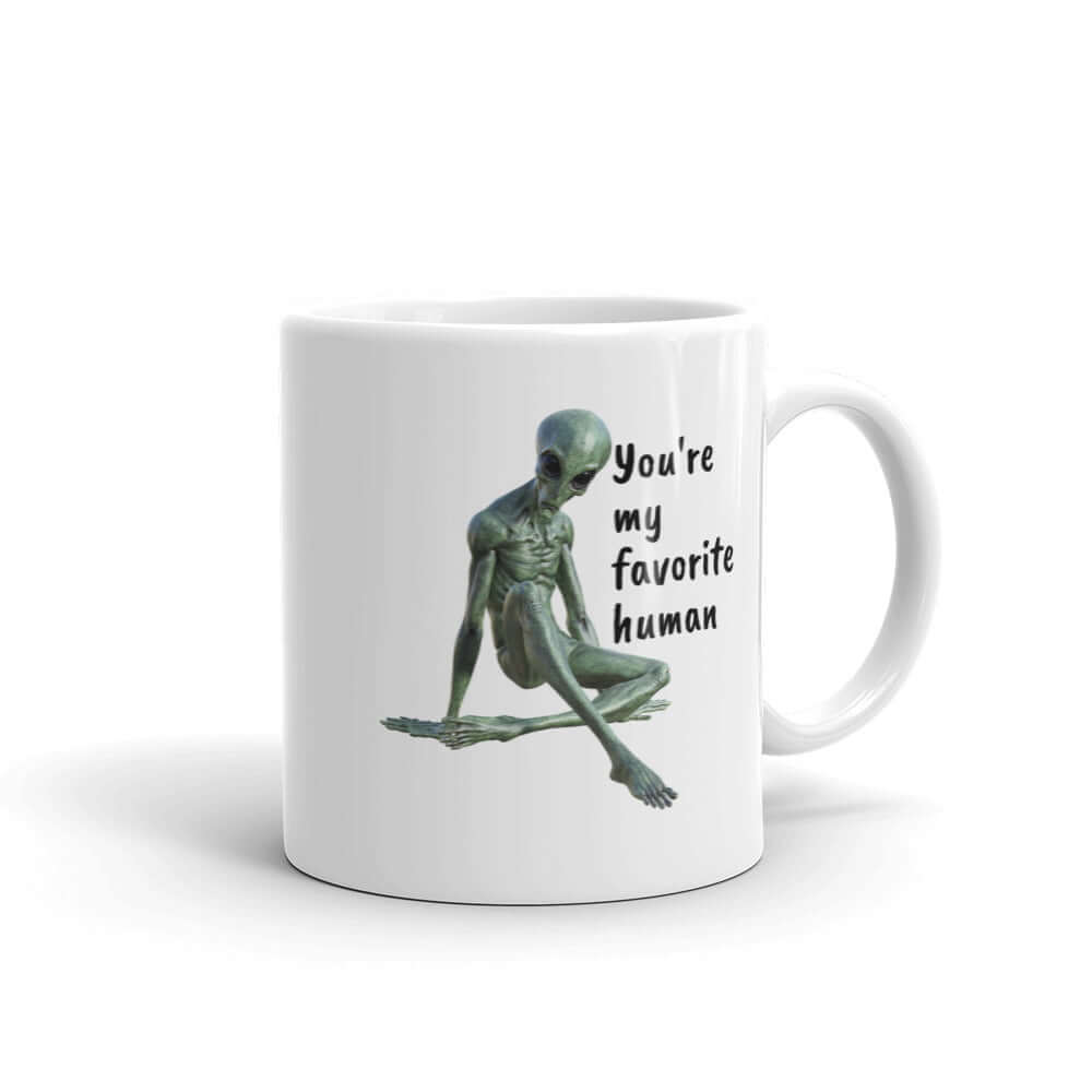 White ceramic coffee mug with funny image of an alien lounging and the words You're my favorite human printed on both sides of the mug.