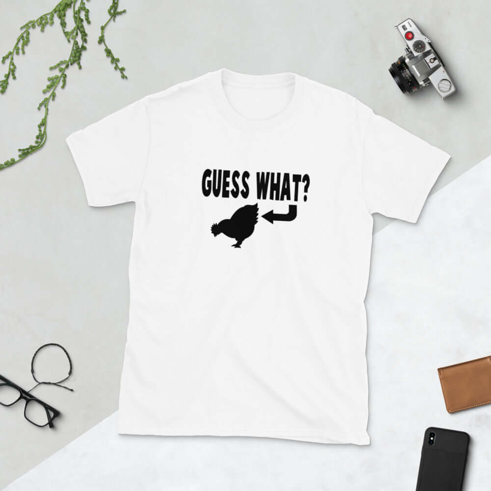 White t-shirt with an image of a chicken and the words Guess what question mark. There is an arrow pointing to the chickens butt. The graphics are printed on the front of the shirt.