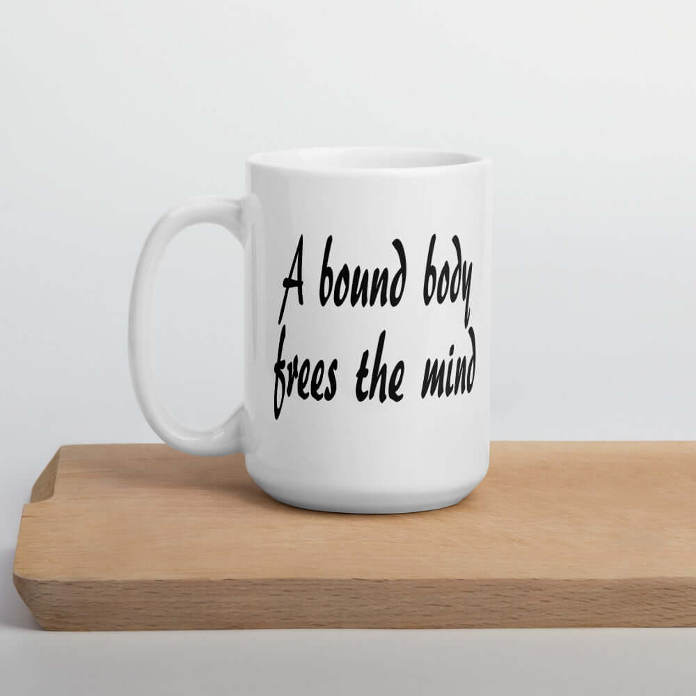 White ceramic coffee mug with the BDSM phrase A bound body frees the mind printed on both sides of the mug.
