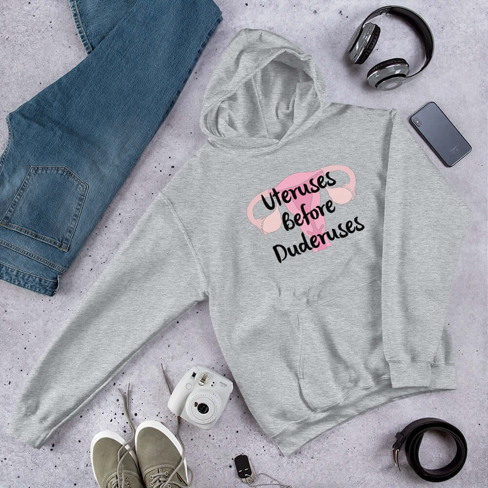 Light grey hoodie sweatshirt with image of a uterus and the words Uteruses before duderuses printed on the front.