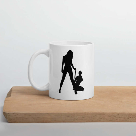 White ceramic coffee mug with a silhouette image of 2 women in a lesbian BDSM scene. 1 woman is on her knees and the other has her on a leash. The graphic is printed on both sides of the mug.