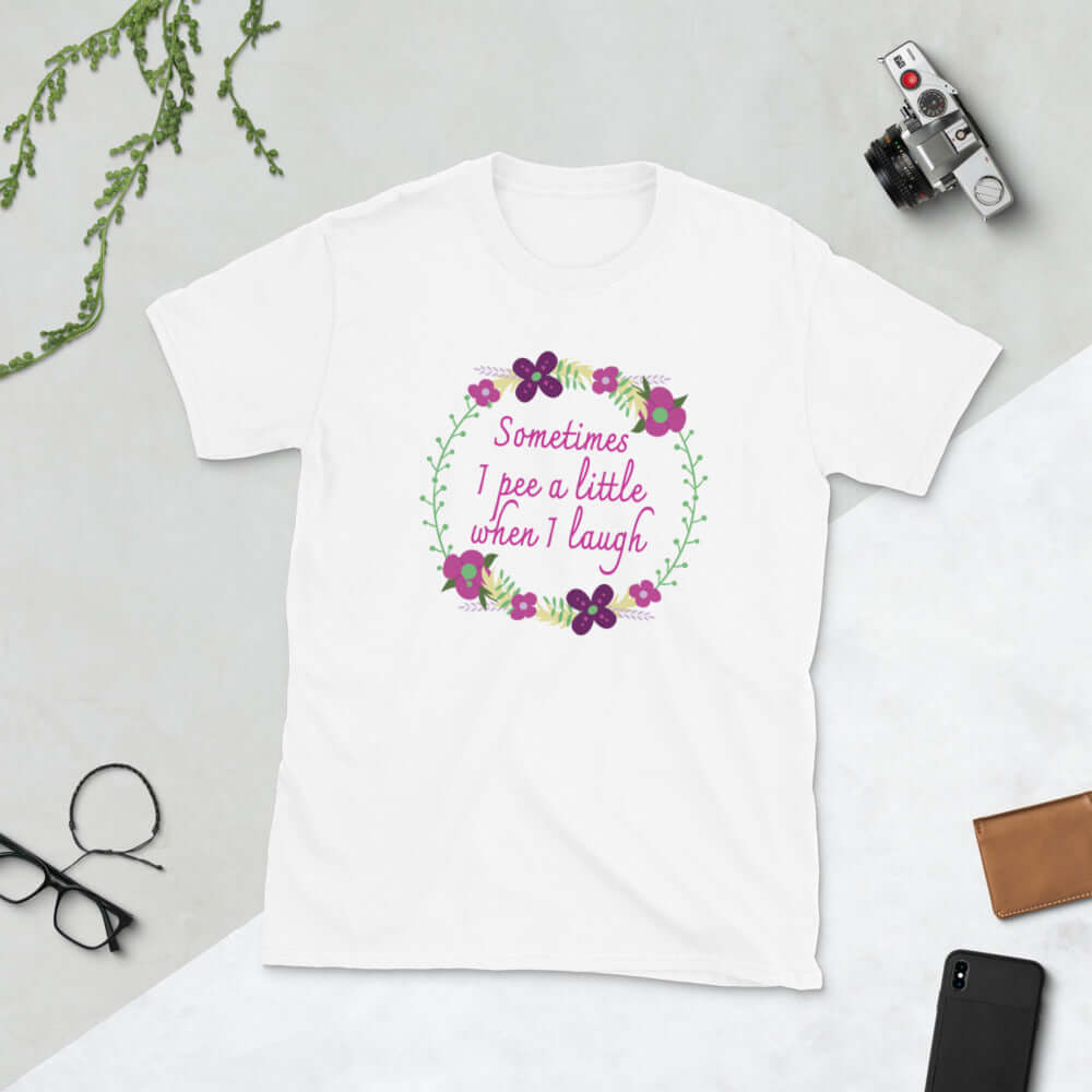 White t-shirt that has a minimalistic style line drawing floral wreath with the phrase Sometimes I pee a little when I laugh printed in the center of the wreath. The graphics are printed on the front of the shirt.