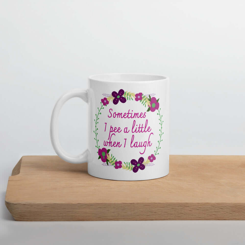 White ceramic coffee mug that has a minimalistic style line drawing floral wreath with the phrase Sometimes I pee a little when I laugh printed in the center of the wreath. The graphics are printed on both sides of the mug.