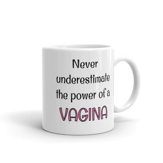 White ceramic coffee mug with the phrase Never underestimate the power of a vagina. The words vagina is pink, the rest of the text is black. The graphics are printed on both sides of the mug.