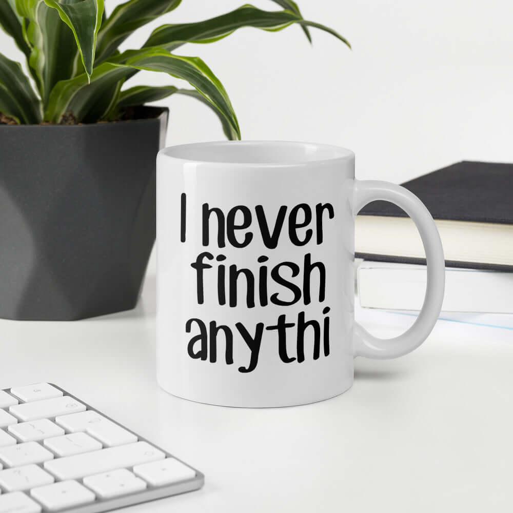 White ceramic coffee mug with the phrase I never finish anything printed on both sides. The letters n and g are missing from the word anything.