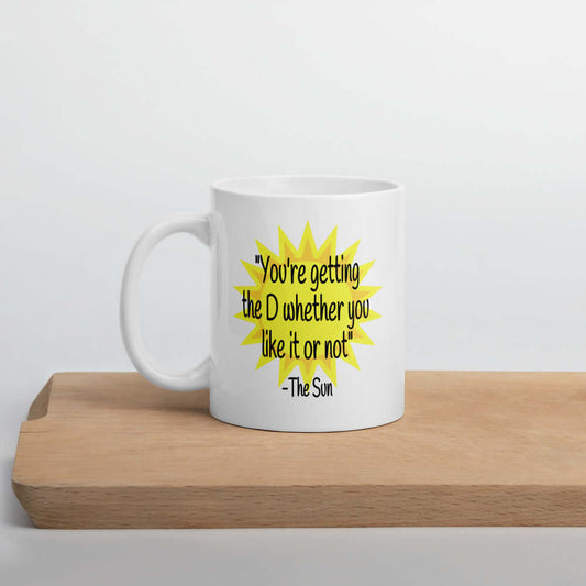 White ceramic coffee mug with image of the sun and the quote You're getting the D whether you like it or not printed on both sides of the mug.