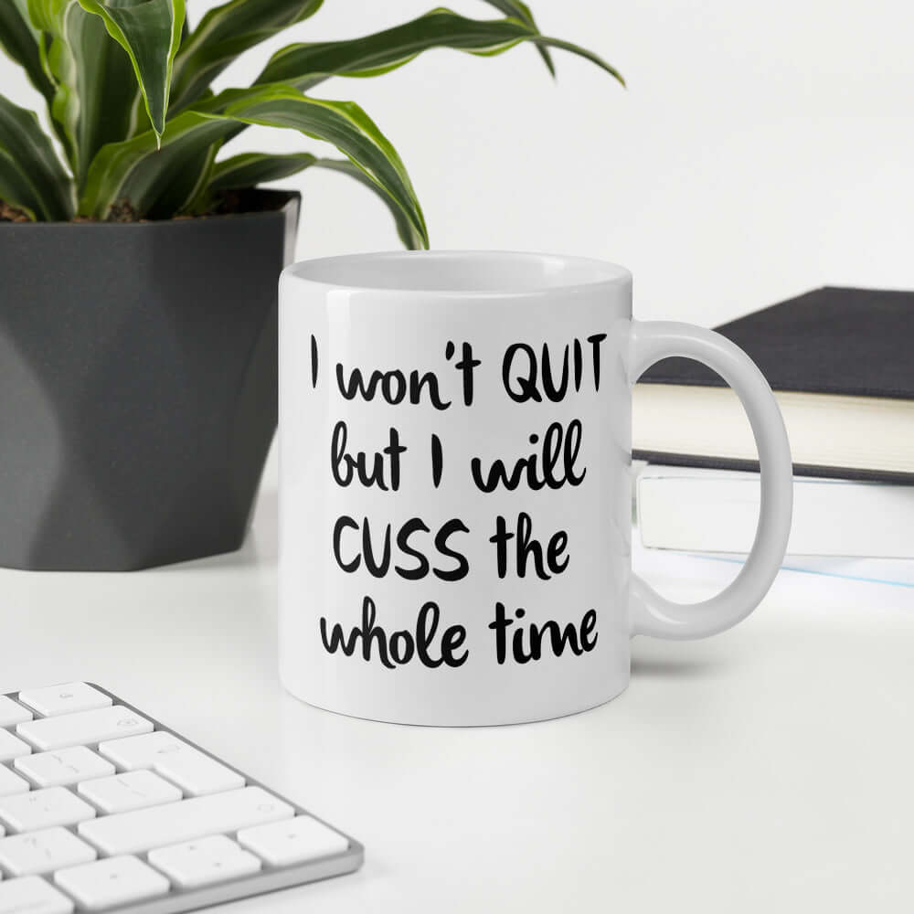 White ceramic mug with the phrase I won't quit but I will cuss the whole time printed on both sides of the mug.