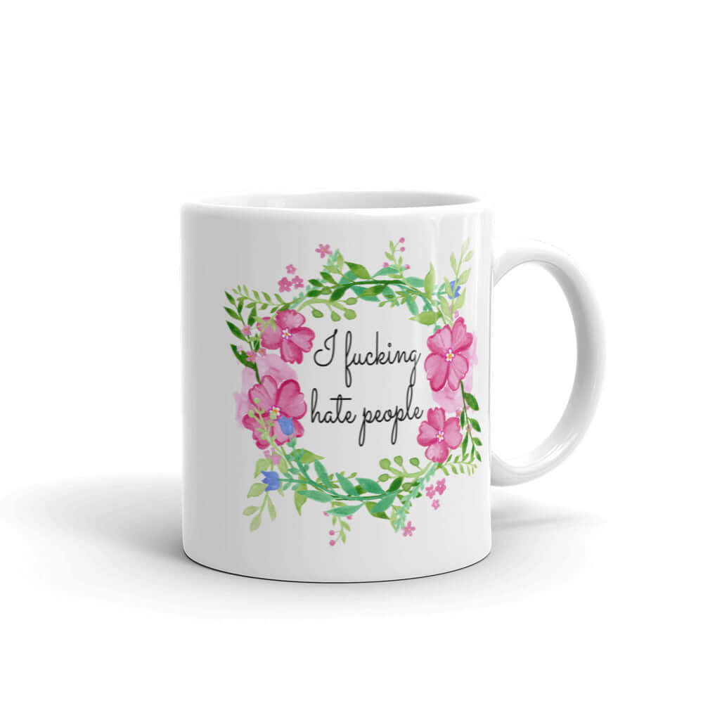White ceramic mug with pink and green floral wreath image and the words I fucking hate people printed on both sides.