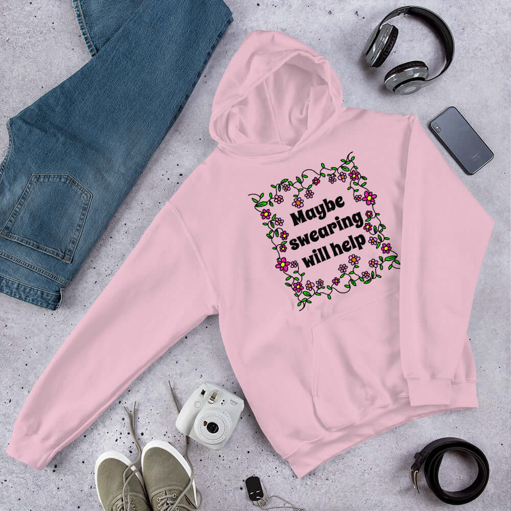Light pink hoodie sweatshirt with a floral graphic and the phrase Maybe swearing will help printed on the front.