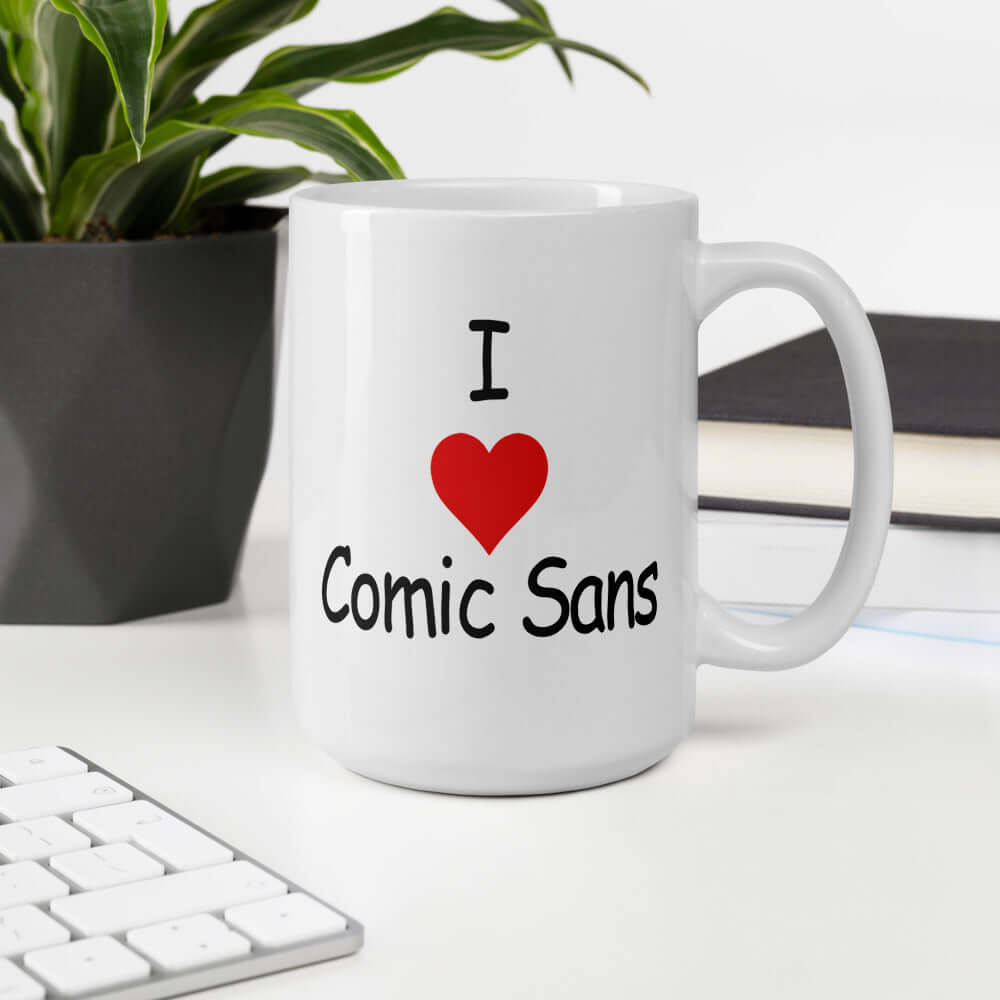 White ceramic coffee mug that says I heart Comic Sans on both sides of the mug. The text is in comic sans font.