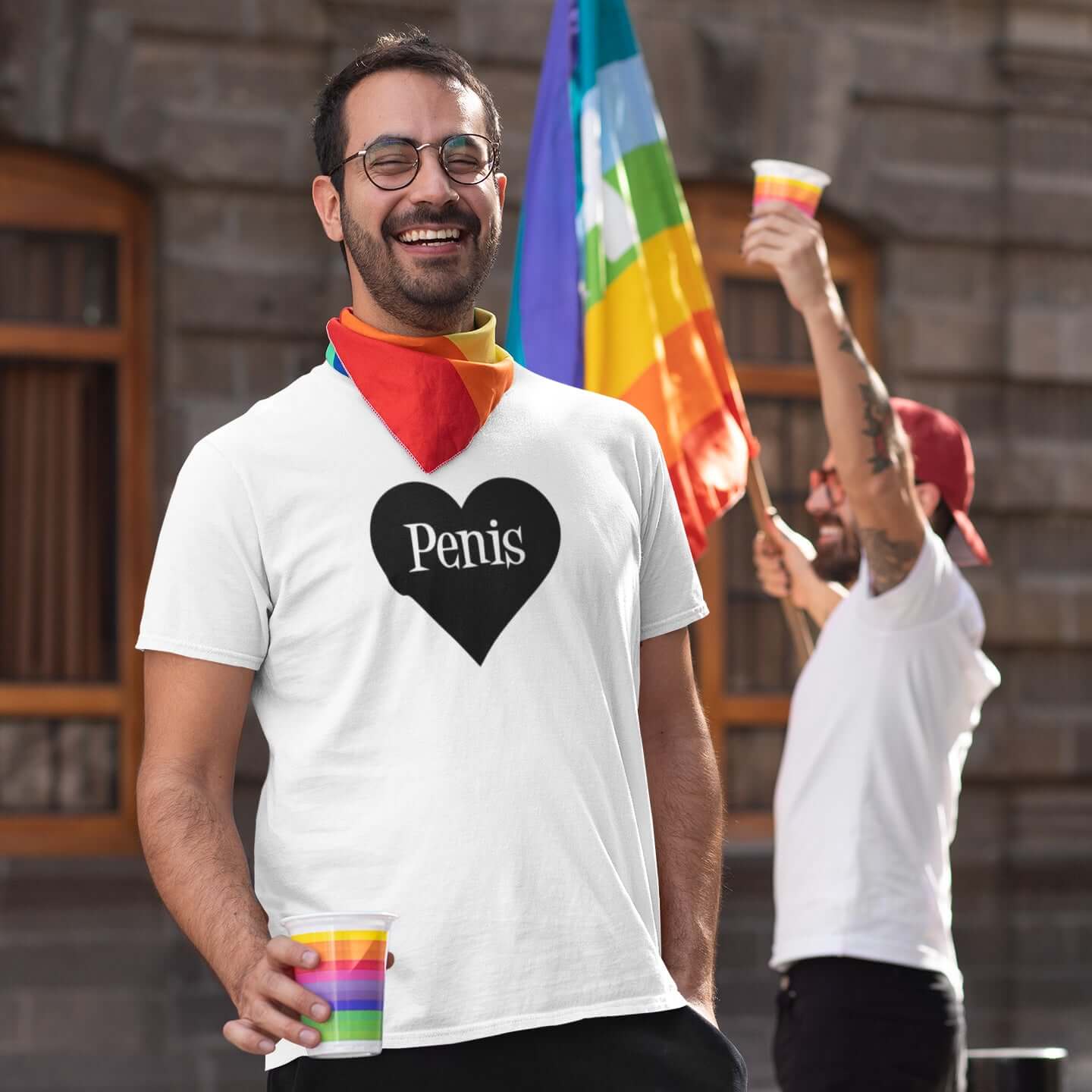 Man at a Pride event wearing a white t-shirt with a heart image printed on the front. The word penis is inside the heart