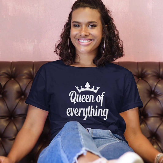 Woman lounging on the sofa wearing a navy blue t-shirt with an image of a crown and the phrase Queen of everything printed on the front of the shirt.