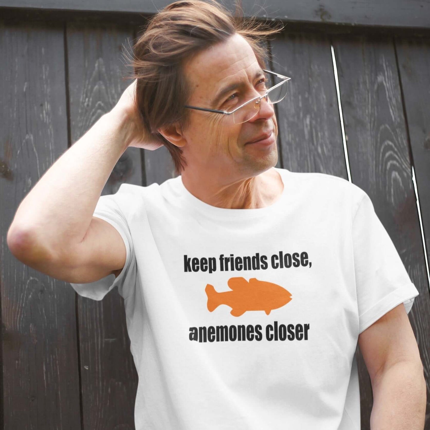 Man wearing white t-shirt with the pun phrase Keep friends close, anemones closer with an image of an orange fish.