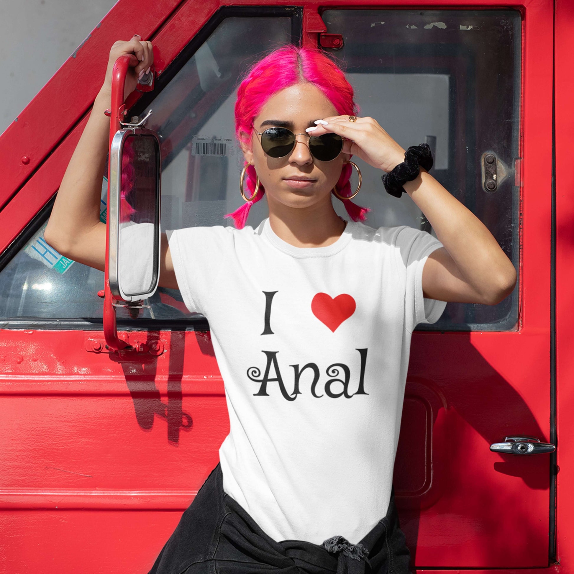 Woman with pink hair wearing a white t-shirt with the words I heart anal printed on the front. The heart is red.