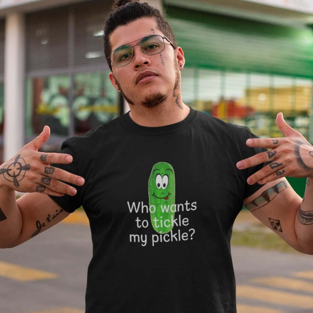 Macho looking man wearing a black t-shirt with an image of a pickle printed on the front. The words Who wants to tickle my pickle are printed under the pickle.