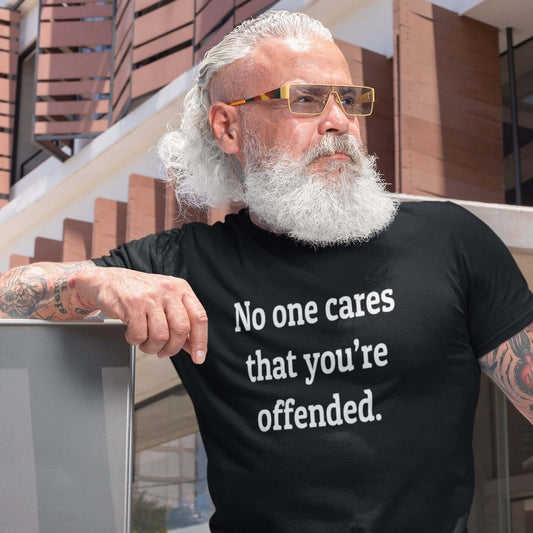 Tattooed bearded man wearing black t-shirt with the words No one cares that you're offended printed on the front.