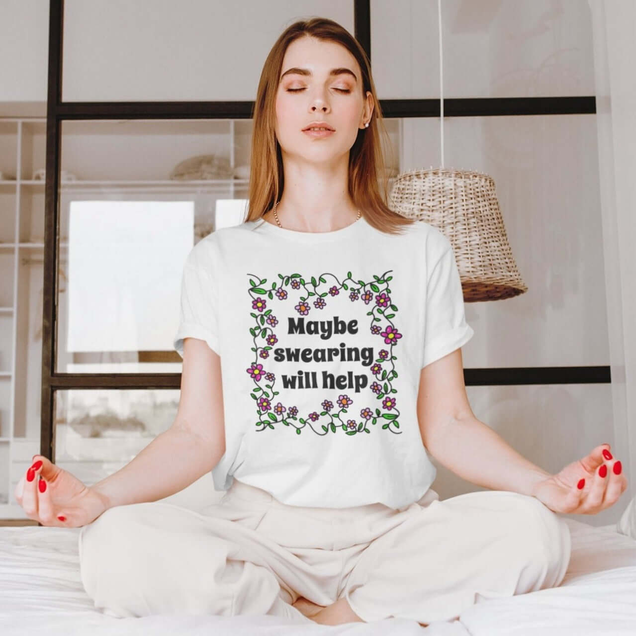 Woman meditating while wearing a white t-shirt with a floral graphic and the phrase Maybe swearing will help printed on the front.