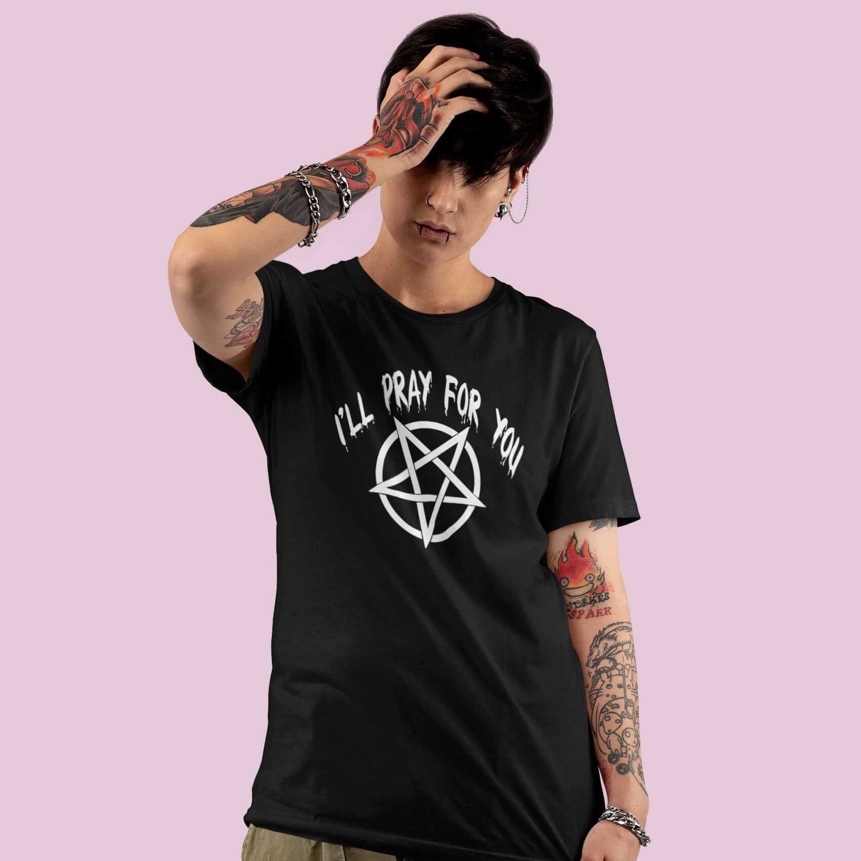 Edgy looking short haired woman wearing black t-shirt with image of a pentagram and the words I'll pray for you printed on the front.