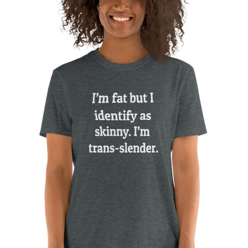 Smiling woman wearing a dark heather grey t-shirt with the phrase I'm fat but I identify as skinny. I'm trans-slender printed on the front.