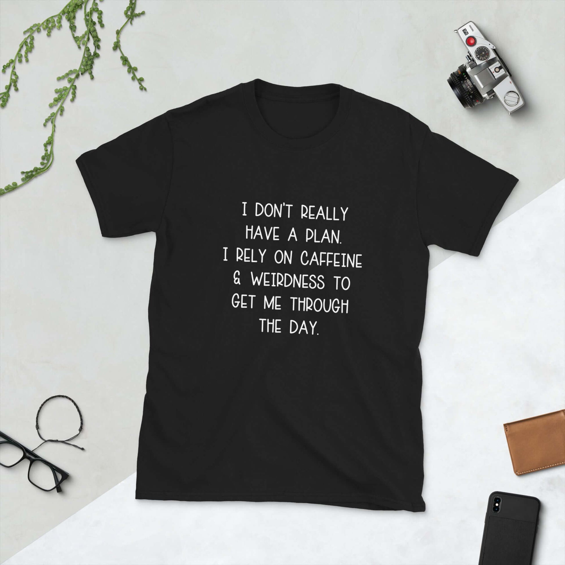Black t-shirt with the words I don't really have a plan. I rely on caffeine & weirdness to get me through the day printed on the front.