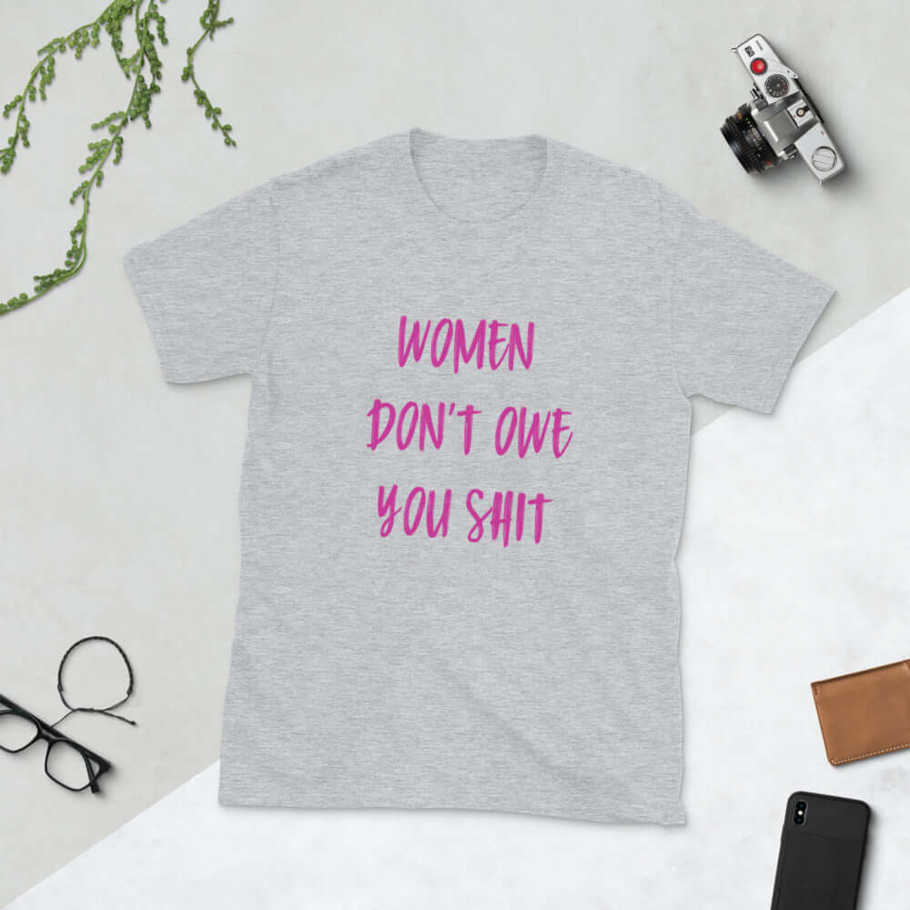 Light grey t-shirt with the words Women don't owe you shit printed on the front in pink.